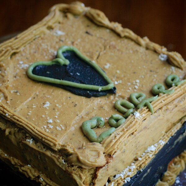 Square cake with brown icing, decorated with a black icing heart, and the word 'coffee' spelled out with green icing.