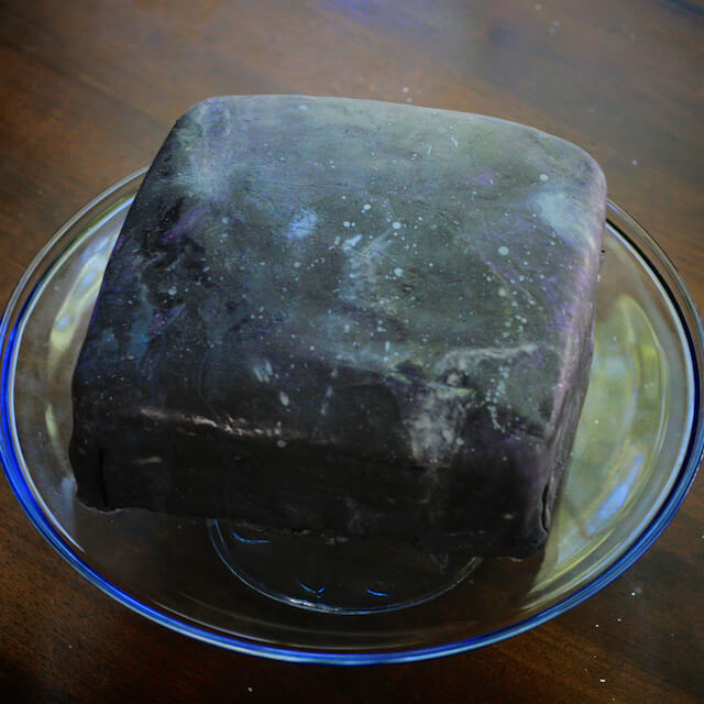 Square cake with black fondant decorated to look like outer space with galaxies, comets, and stars.