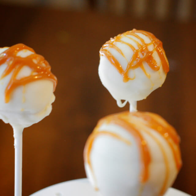 Three white chocolate covered cake pops with a caramel drizzle and a sprinkle of salt.