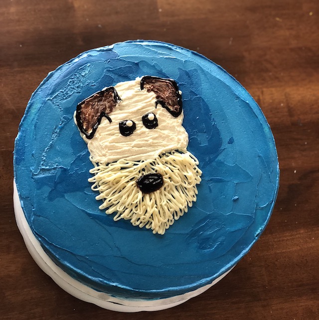 Round vanilla cake with blue icing decorated with a white puppy face
