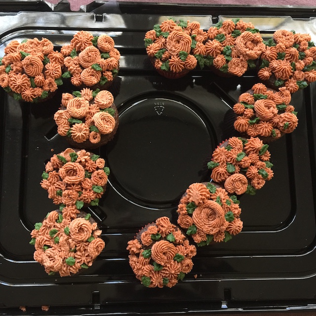 The number seventeen formed with cupcakes decorated with pink flowers.