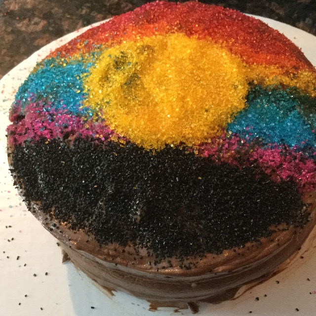 Round triple chocolate cake decorated with sprinkles to look like a sunset.